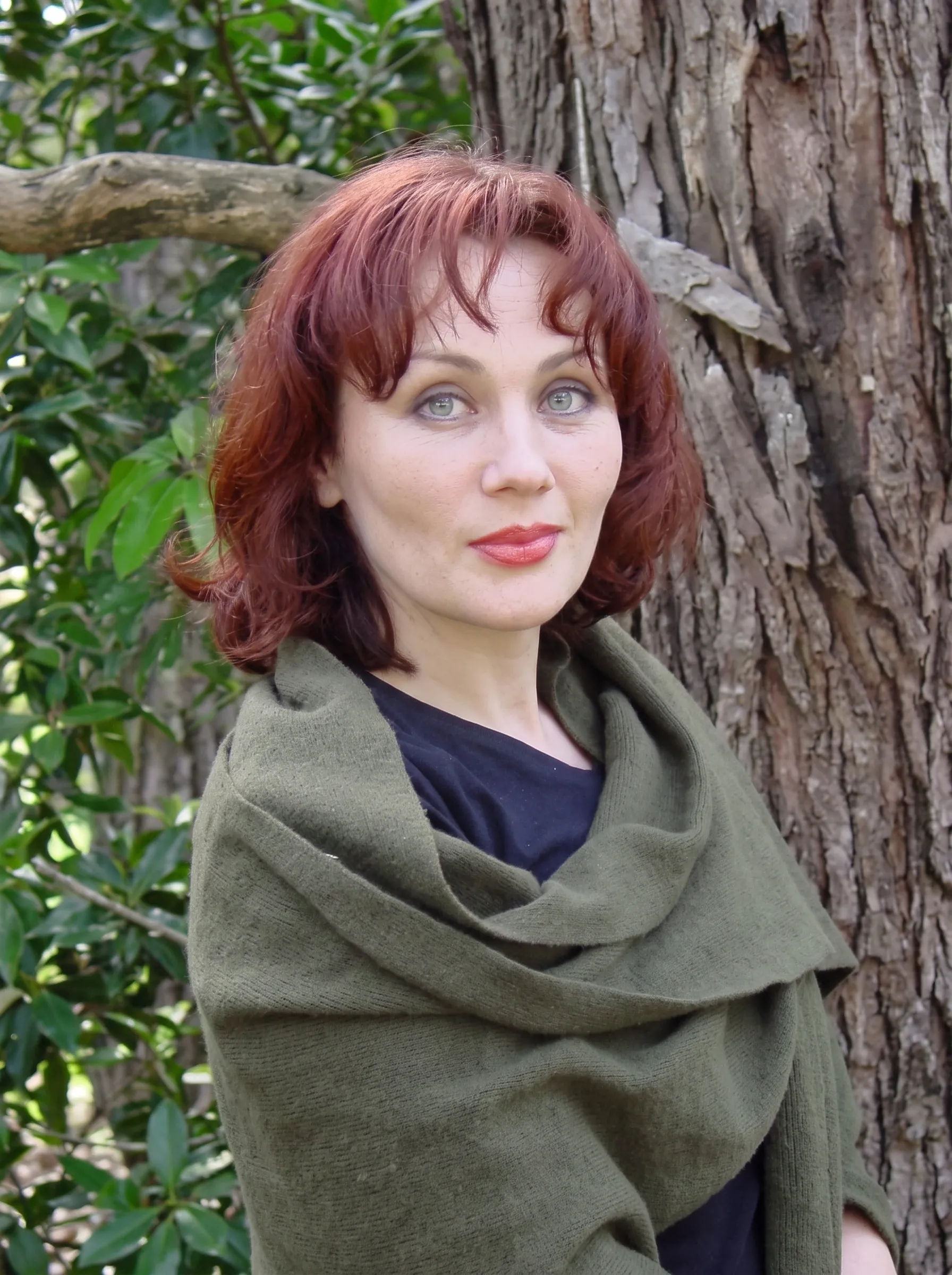 Portrait of the artist Dinara Dindarova, wearing an olive wrap, standing beside a tree